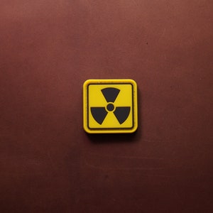 Peut inclure: Un patch carré jaune avec un symbole de radiation noir. Le patch est fait d'un matériau ressemblant à du caoutchouc.