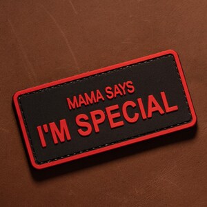 Op de afbeelding: Een rechthoekige patch met een zwarte achtergrond en een rode rand. De tekst MAMA SAYS I'M SPECIAL is in rode letters in het midden van de patch gedrukt. Het ontwerp heeft strakke, gedurfde lijnen en een hoog contrast in kleur.