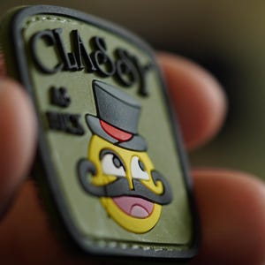 Könnte beinhalten: Ein grüner und schwarzer Patch mit dem Text "CLASSY & NICE" und einem Cartoon-Bild eines lächelnden Gesichts mit Zylinder und Schnurrbart.