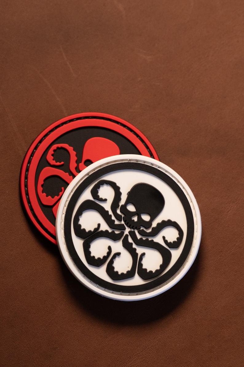 May include: Two circular patches featuring a raised graphic of a skull with octopus tentacles extending from the base. One patch has a white background with a black skull and tentacles, while the other has a red background with a black skull and tentacles.