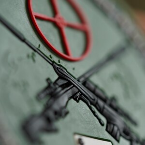May include: A green patch with a red target, two crossed rifles, and a black spade playing card. The text "ACE OF SPADES" is visible at the top of the patch.
