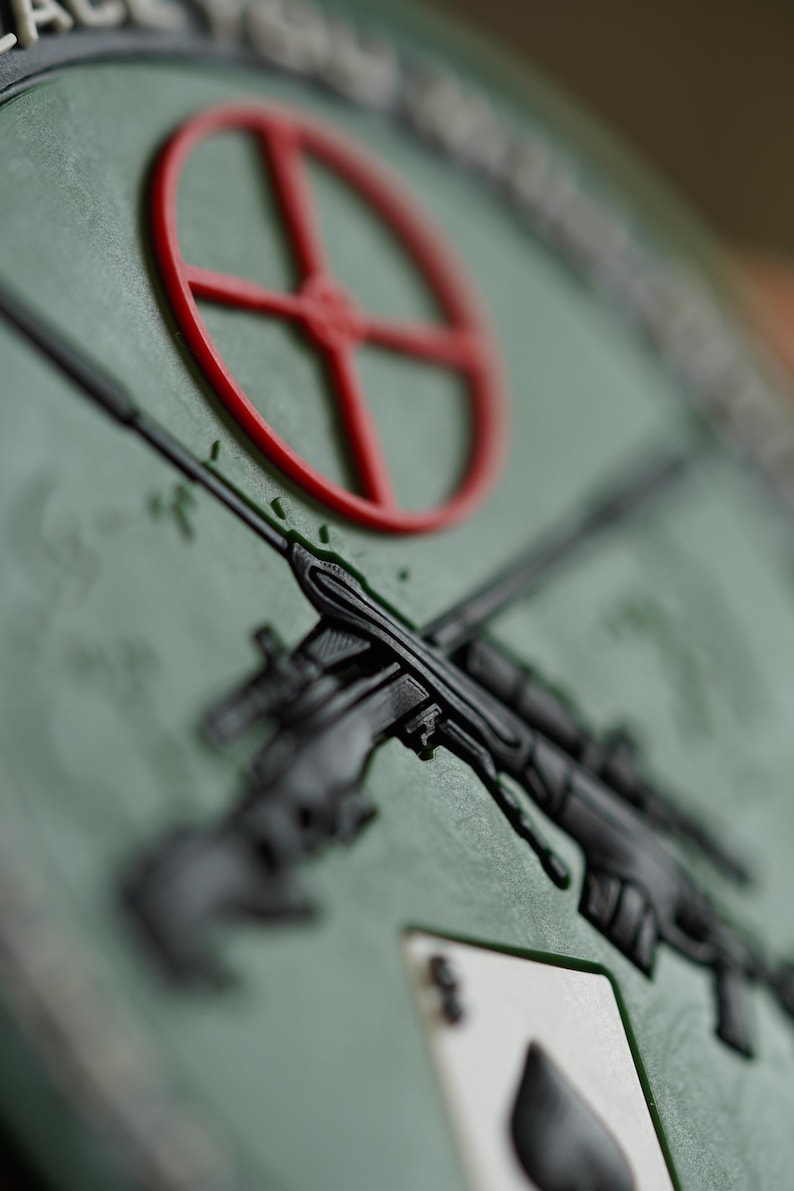 May include: A green patch with a red target, two crossed rifles, and a black spade playing card. The text "ACE OF SPADES" is visible at the top of the patch.