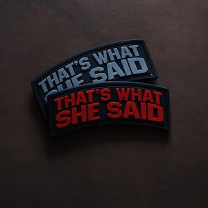 Könnte beinhalten: Zwei schwarze Stoff-Patches mit weißer und roter Beschriftung. Der obere Patch sagt "That's What She Said" in weißer Schrift. Der untere Patch sagt "That's What She Said" in roter Schrift.