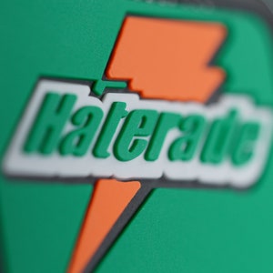 May include: Close-up of a patch with the word "Haterade" in green, white, and orange. The patch has a green background with an orange lightning bolt design. The text is in a 3D style.