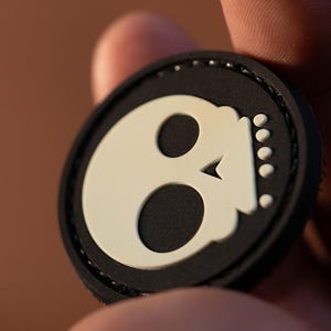 以下が含まれることがあります： 白の輪郭のある黒と白のドクロパッチ。ドクロは小さく、白く、尖った鼻と、ドクロの右側に白い点の列があります。