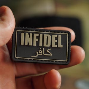 May include: A black patch with the word "INFIDEL" in tan letters and the Arabic word for "infidel" in tan letters below it.