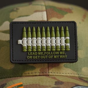 May include: A black and green patch with a row of bullets and the text "Lead me, follow me, or get out of my way".