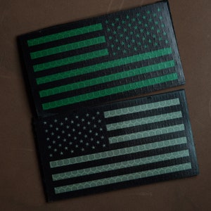 Può includere: Due toppe di bandiera americana con un motivo a nido d'ape. La toppa superiore è verde e nera, e la toppa inferiore è nera e bianca.