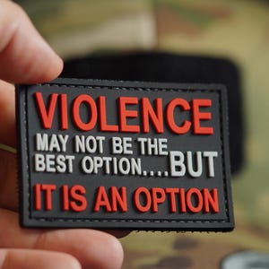 May include: A black rectangular patch with the words "VIOLENCE" in red block letters. Below, the text reads "MAY NOT BE THE BEST OPTION....BUT IT IS AN OPTION" in white and red letters.