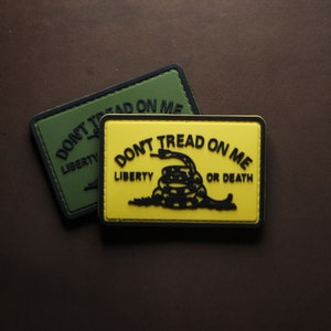 Peut inclure: Deux patchs avec le slogan "Don't Tread On Me" et un serpent à sonnettes enroulé. Le patch du haut est vert avec les mots "Liberty" et "Don't Tread On Me". Le patch du bas est jaune avec les mots "Liberty" et "Don't Tread On Me Or Death".