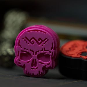 Puede incluir: Un sello de goma en forma de calavera de color rosa brillante con un patr&oacute;n decorativo en la frente. El sello est&aacute; hecho de un material suave y flexible y est&aacute; dise&ntilde;ado para proyectos de manualidades y arte.