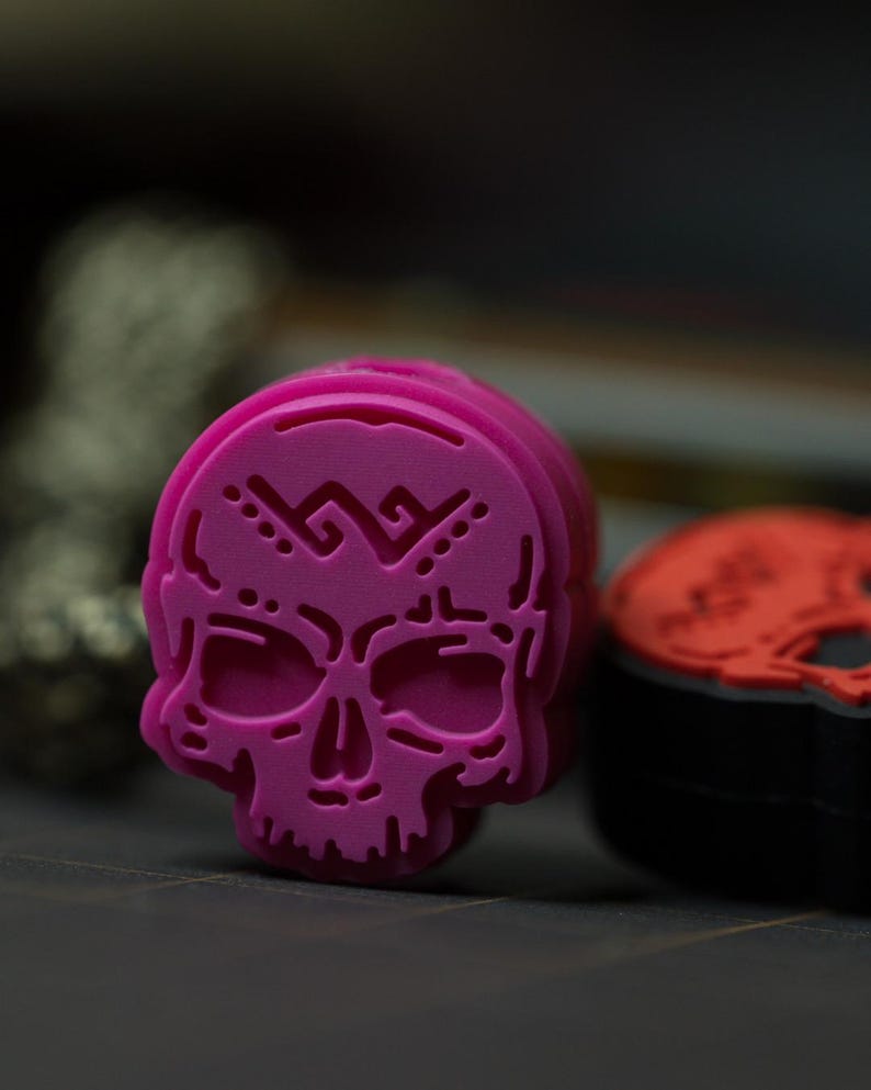 Puede incluir: Un sello de goma en forma de calavera de color rosa brillante con un patr&oacute;n decorativo en la frente. El sello est&aacute; hecho de un material suave y flexible y est&aacute; dise&ntilde;ado para proyectos de manualidades y arte.
