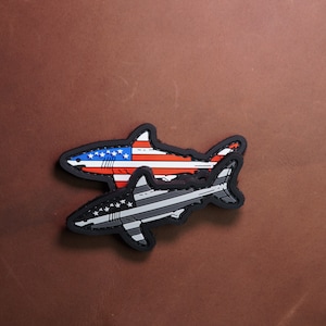 Peut inclure: Deux patchs en forme de requin, l'un avec un motif de drapeau américain et l'autre avec un motif de drapeau de la ligne bleue fine.