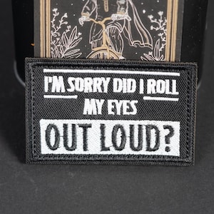 May include: A rectangular black embroidered patch with a white border and white stitched text that reads I'M SORRY DID I ROLL MY EYES OUT LOUD? The patch features a textured fabric surface with bold, capitalised lettering centred on the front.