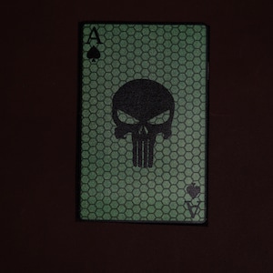 Op de afbeelding: Een groene speelkaart met een zwart schedel- en kruisbeenderontwerp. De kaart is een aas schoppen.