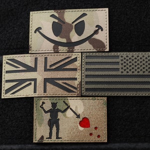 May include: Four black and white embroidered patches on a black background. The patches are a smiley face with a mischievous grin, a Union Jack flag, an American flag, and a pirate with a heart.