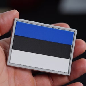 Puede incluir: Un parche bordado azul, negro y blanco con la bandera de Estonia. El parche se sostiene en una mano.