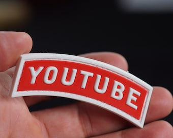 Könnte beinhalten: Weißer Patch mit rotem Rand und dem Wort "YOUTUBE" in weißen Buchstaben.