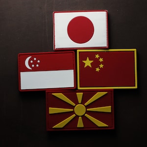 Puede incluir: Cuatro parches bordados con las banderas de Japón, Singapur, China y Macedonia del Norte. Los parches son rojos, blancos y amarillos.