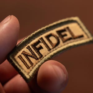 May include: A tan and green fabric patch with the word "INFIDEL" embroidered in brown thread.