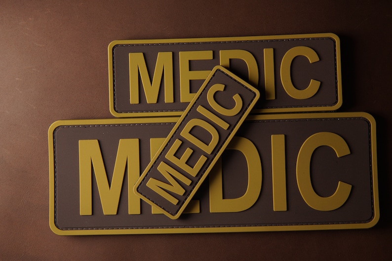 Pu&ograve; includere: Tre toppe marroni con cuciture gialle e la parola "MEDIC" stampata in lettere gialle.