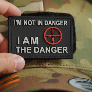 May include: Black patch with white text that reads "I'm not in danger I am the danger" with a red target symbol in the middle.