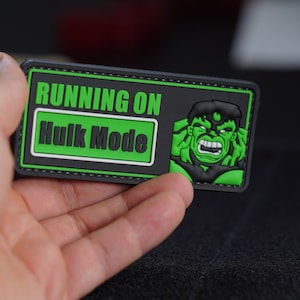 Puede incluir: Un parche bordado negro y verde con el texto "RUNNING ON HULK MODE" y una imagen verde de Hulk.