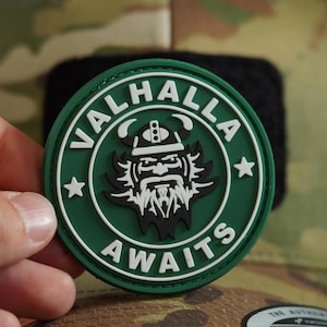 May include: A green and white circular patch with the text "Valhalla Awaits" and a cartoon image of a Viking with a beard and helmet. The patch has a white star on each side of the text.