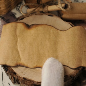 Op de afbeelding: Een bruine papieren rol met een licht verbrande rand, rustend op een houten schijf. De rol is leeg en klaar om te beschrijven.