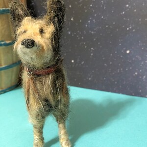 Puede incluir: Figura de perro en miniatura hecha a mano, con pelaje marr&oacute;n y beige, orejas negras y collar rojo. El perro est&aacute; sobre una superficie azul claro. El fondo presenta un dise&ntilde;o de noche estrellada. Aspecto texturizado y detallado.