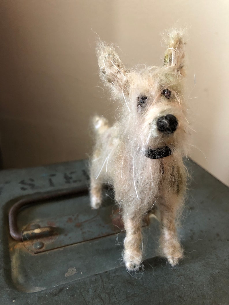 Puede incluir: Figura de perro terrier hecha a mano, de color blanquecino, con nariz y collar negros. El perro tiene un aspecto peludo y texturizado y est&aacute; sobre una superficie met&aacute;lica verde desgastada. Las orejas del perro est&aacute;n erguidas y sus ojos son oscuros.