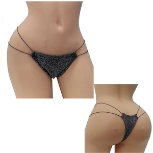May include: Black glittery thong bikini bottoms with thin straps. The bikini bottoms are displayed on a mannequin, showcasing the front and back views. The fabric has a sparkly texture, catching the light.