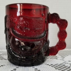 May include: A red glass mug with a textured design and a knobbed handle. The mug has a dark red color and a glossy finish.