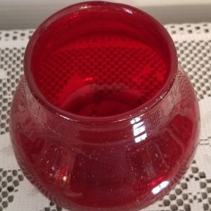 May include: A deep red glass vase with a textured, bubbled surface. The vase has a wide mouth and a rounded body.