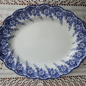 May include: Oval serving platter with a white center and a blue floral border. The scalloped edge is adorned with blue flowers and foliage. This vintage-style dish is perfect for serving food.