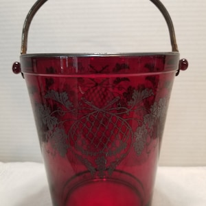 May include: A red glass ice bucket with a silver-toned metal handle and a silver-toned floral design.
