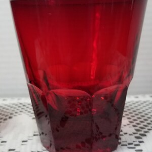 May include: A red glass shot glass with a faceted design. The glass is clear and has a smooth, polished finish.