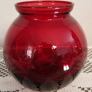 May include: A round, red glass vase with a wide mouth. The vase has a slight ombre effect, with a darker red at the bottom.