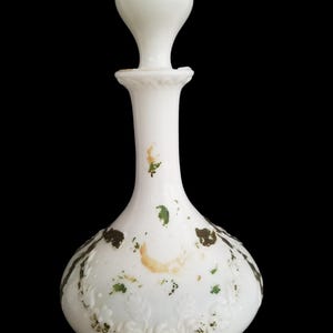 May include: White glass bottle with a round, bulbous stopper. The bottle has a floral design and green and brown stains.