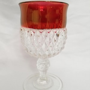May include: A clear glass goblet with a diamond pattern and a red rim. The goblet has a stem and a round base.