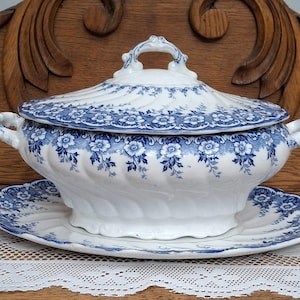 May include: A white and blue floral patterned tureen with a matching lid and serving plate. The tureen has handles on either side and a decorative handle on the lid. The floral pattern is a classic design.
