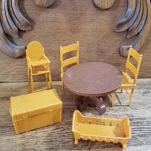 May include: A miniature dollhouse furniture set featuring a round brown table, three yellow chairs, a high chair, a trunk, and a crib. The set is made of plastic and is designed for children's play.