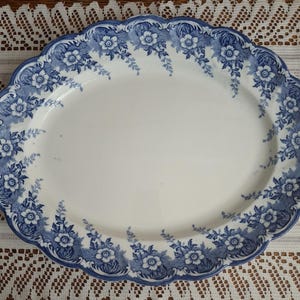 May include: Oval serving platter with a white center and a blue floral design around the scalloped edge. The blue pattern includes flowers and foliage. The platter is likely made of ceramic or porcelain.