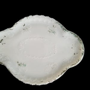 May include: White ceramic serving tray with a scalloped edge and intricate floral designs. The tray has a slightly distressed look, with hints of green and gold.