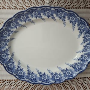May include: Oval serving platter with a white center and a blue floral border. The rim has a scalloped edge. The blue floral design includes flowers and leaves. The platter is made of ceramic.