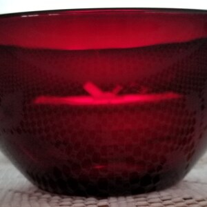 May include: A deep red glass bowl with a textured surface. The bowl is empty and appears to be made of heavy glass.