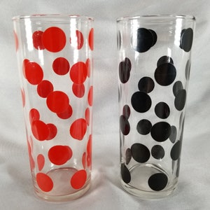 May include: Two clear glass drinking glasses with a polka dot pattern. One glass has red polka dots and the other has black polka dots.