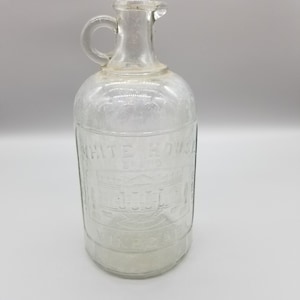 May include: A clear glass bottle with a handle, embossed with the text "White House Vinegar".
