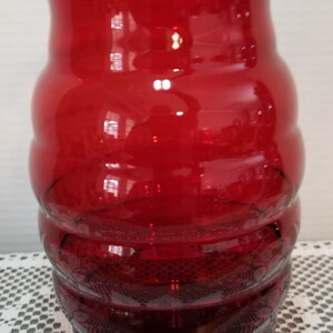 May include: A red glass vase with a ruffled top and a textured, ribbed design. The vase is clear and has a slight amber hue.