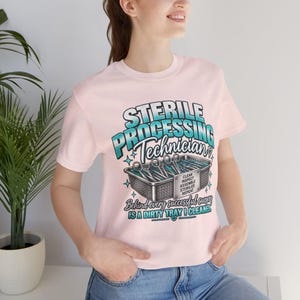 Könnte beinhalten: Ein hellrosa T-Shirt mit kurzen Ärmeln und einem Aufdruck mit dem Text "STERILE PROCESSING TECHNICIAN" sowie "Behind every successful surgery IS A DIRTY TRAY I CLEANED." Die Grafik zeigt einen Metallkorb voller chirurgischer Instrumente.